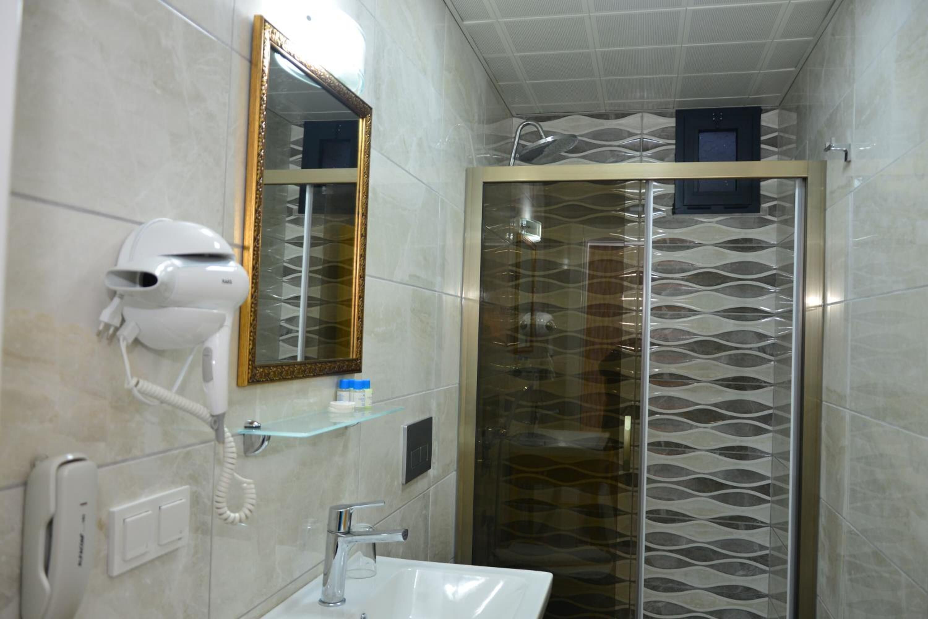 A bathroom with a hairdryer, a mirror, a glass shower enclosure, and a sink.
