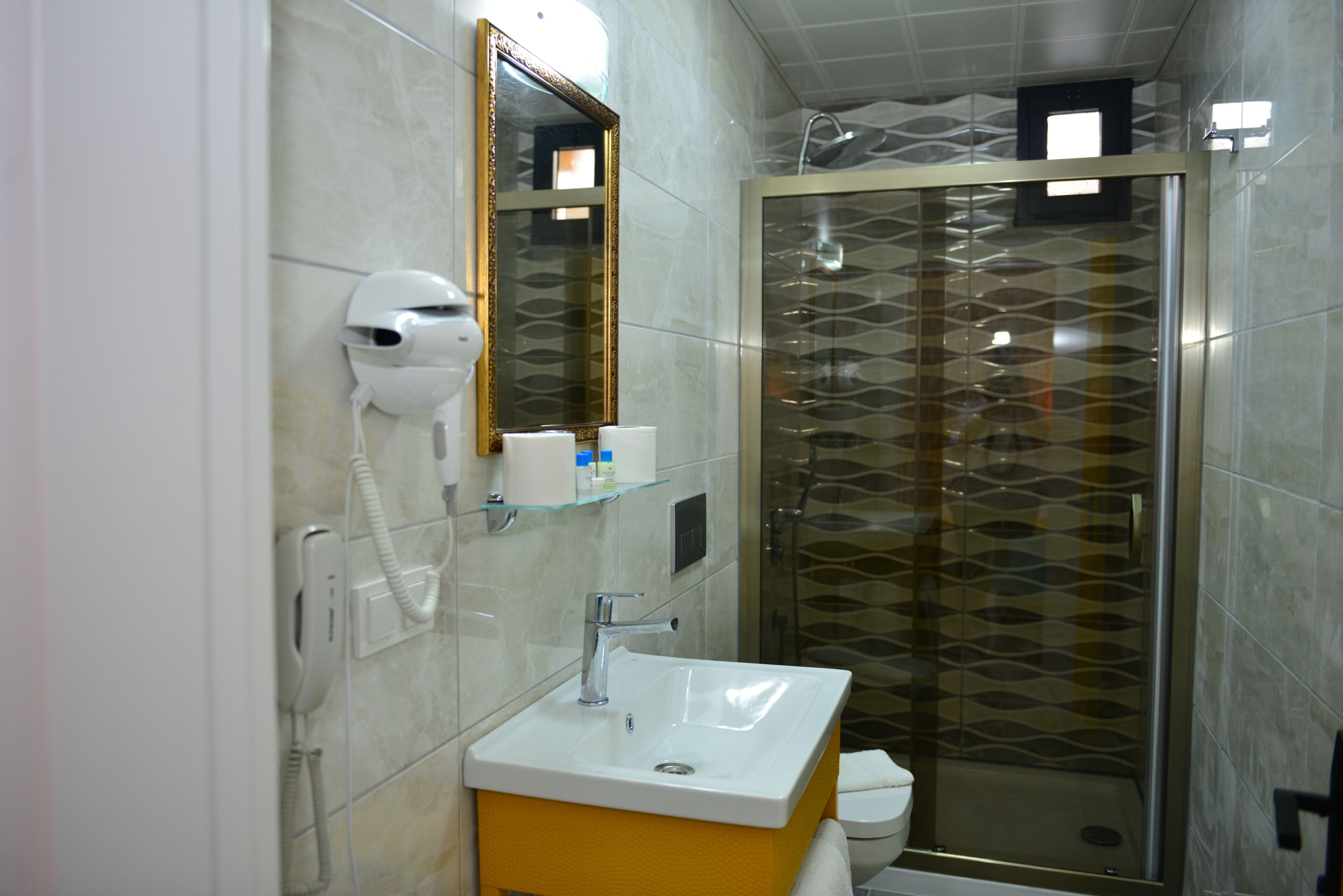 A bathroom with a white sink, a mirror, a hairdryer, and a shower with patterned glass doors.