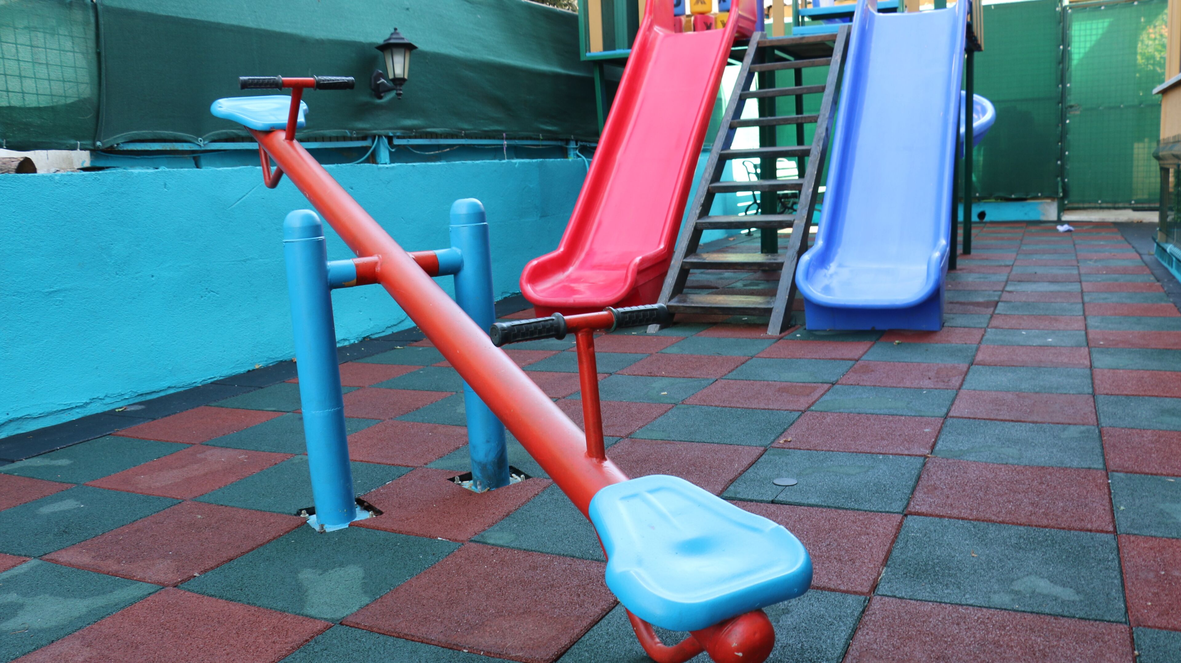 A playground with a seesaw, two slides, and a climbing ladder.