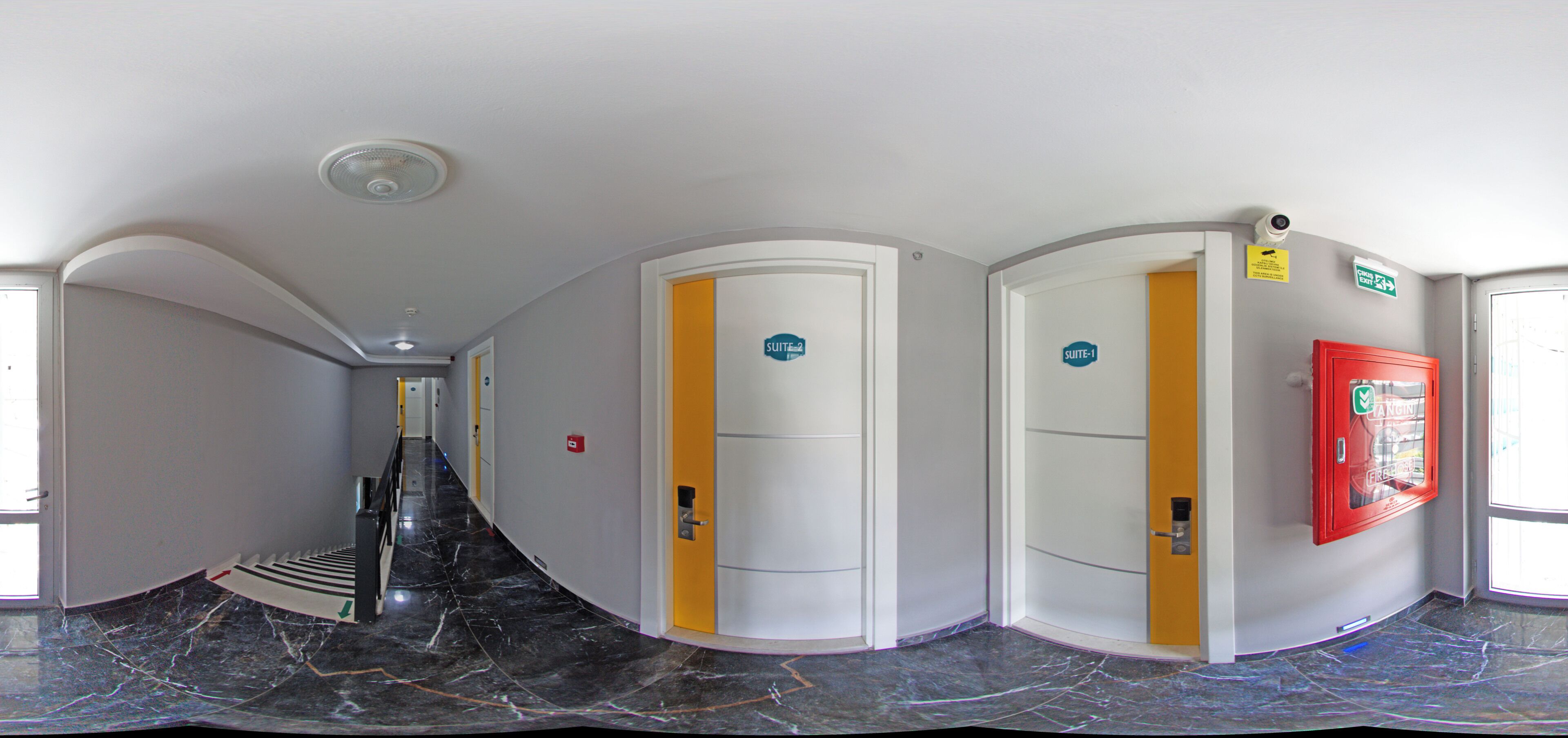 A hotel hallway with curved walls, doors labeled 'Suite-1' and 'Suite-2', a red vending machine, and a security camera.