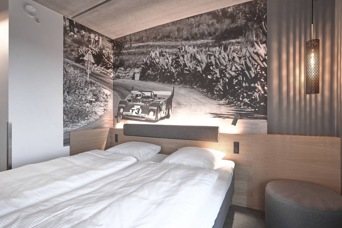 Une chambre moderne avec un grand lit, une tête de lit dotée d’une étagère intégrée et une lampe fixée au mur.