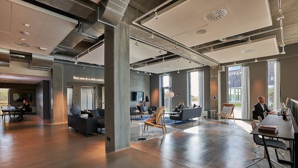 A spacious, modern office with a mix of seating areas and a long table for meetings.
