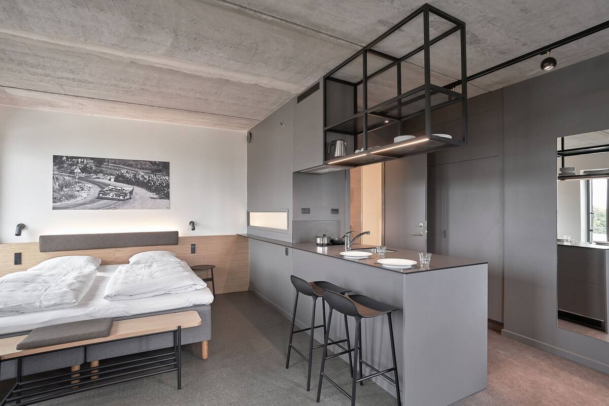 Une chambre d’hôtel moderne et compacte, dotée d’un lit, d’une petite kitchenette et d’un grand miroir.