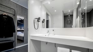 A modern bathroom with a white sink, a mirror, and a shower area.