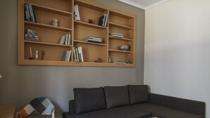 Uma sala de estar moderna com um sofá cinza escuro, uma estante de madeira e uma cadeira estampada.