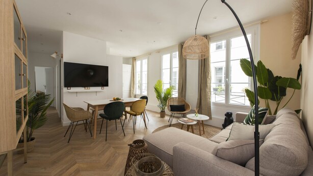 Una sala de estar moderna con un sofá, una mesa de comedor, sillas y un televisor montado en la pared.