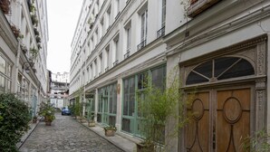 Una calle adoquinada flanqueada por edificios con balcones, plantas en macetas y una puerta de madera.
