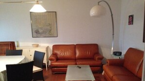A living room with a brown leather sofa, a white coffee table, a dining table with chairs, and a lamp.