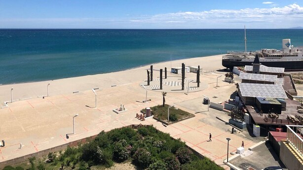 A coastal area with a beach, a promenade, and a building with a helipad.