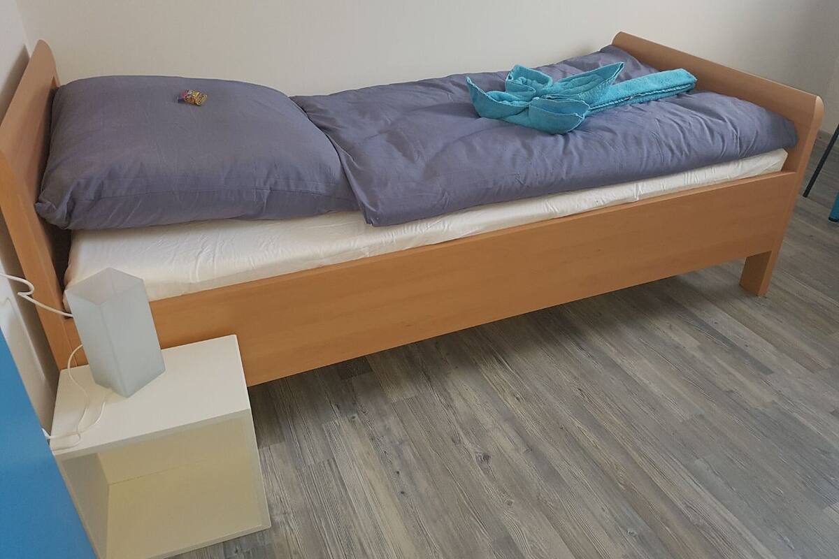 A single bed with a wooden frame, grey bedding, and a blue towel.