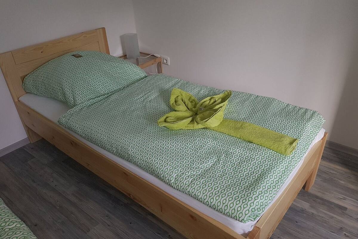 A single bed with a green patterned bedspread, a yellow towel, and a wooden headboard.
