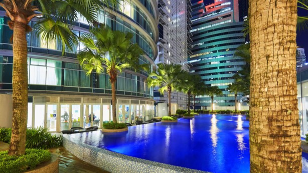 A modern hotel with a large indoor swimming pool, palm trees, and a view of high-rise buildings at night. - Yemala Suites @ Vortex KLCC (Kuala Lumpur)