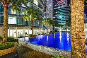 A modern hotel with a large indoor swimming pool, palm trees, and a view of high-rise buildings at night. - Yemala Suites @ Vortex KLCC (Kuala Lumpur)
