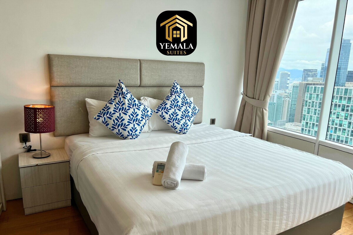A hotel room with a bed, a nightstand, a lamp, and a view of the city.
