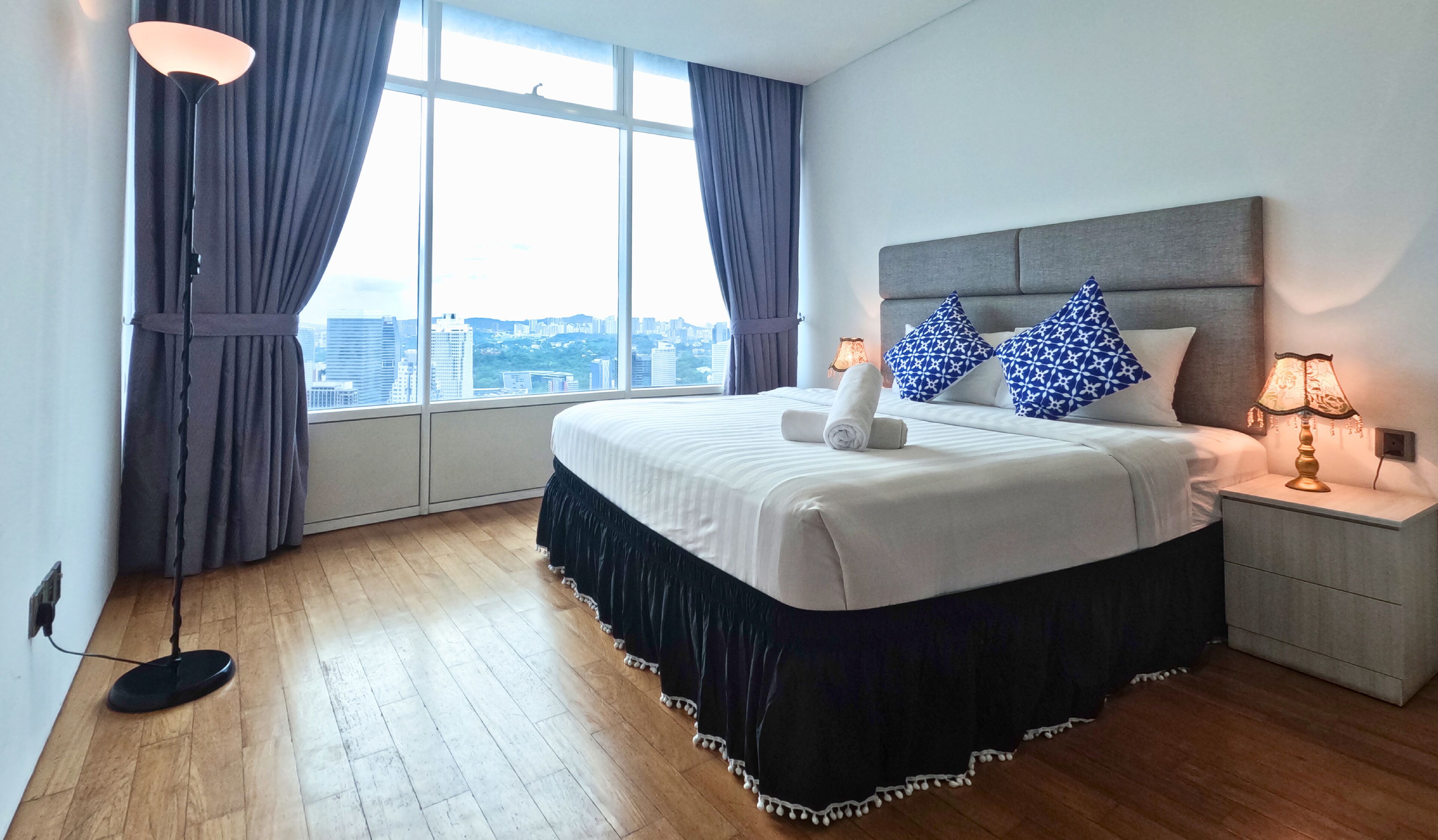 Une chambre d’hôtel avec un grand lit, une table de chevet, une lampe et une vue sur la ville par une grande fenêtre.