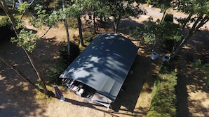 An aerial view of a covered outdoor area with a table and chairs, surrounded by trees and a gravel path.
