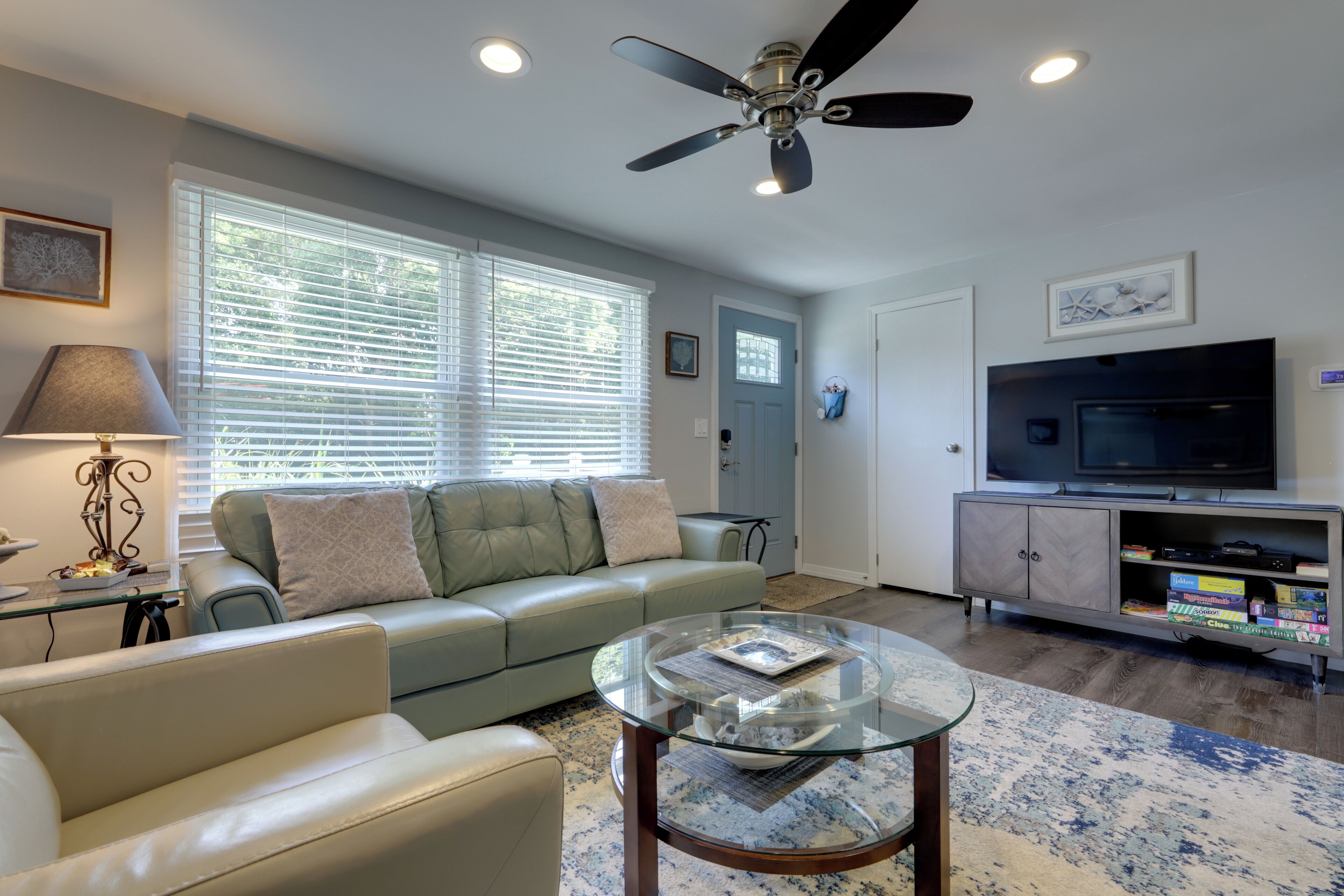 A living room with a sofa, a glass coffee table, a television, and a ceiling fan.
