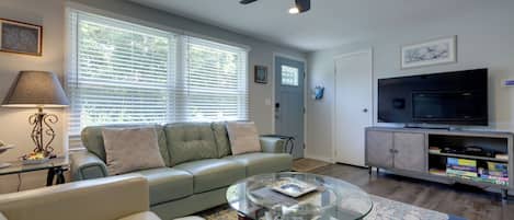A living room with a sofa, a glass coffee table, a television, and a ceiling fan.