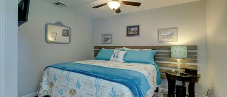 A bedroom with a bed, a ceiling fan, a bedside table with a lamp, and framed pictures on the wall.