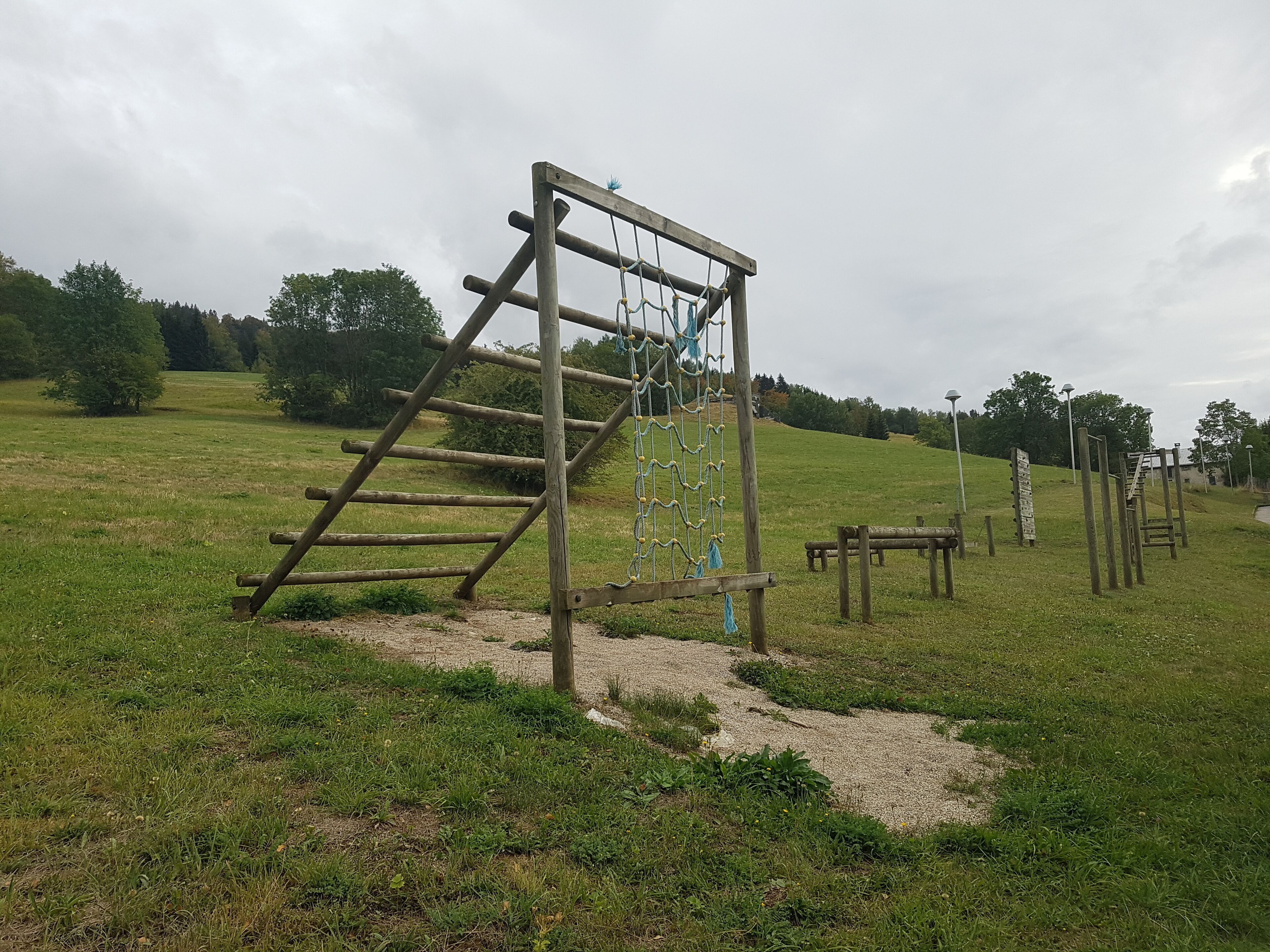 A playground with wooden climbing structures and a rope ladder in a grassy field.