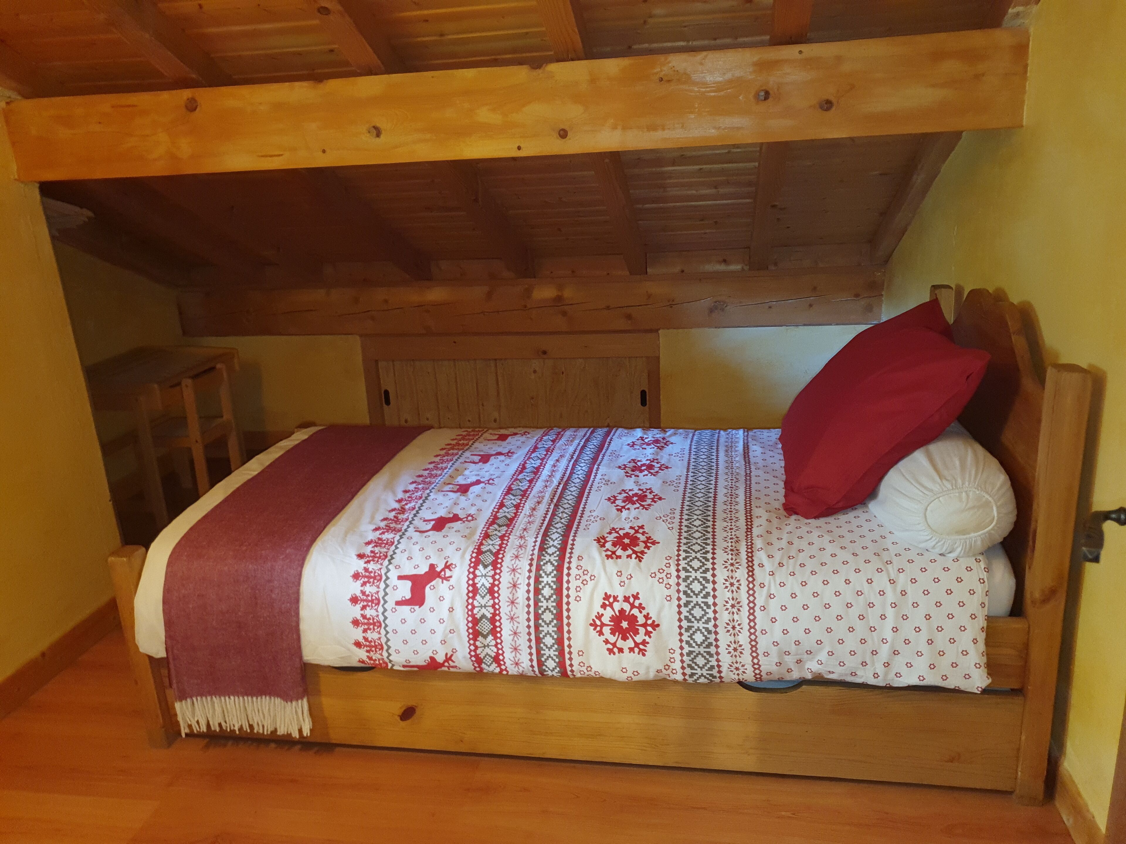A wooden bed with a patterned bedspread, a red pillow, and a wooden headboard.
