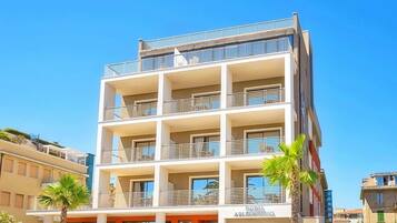 Un hotel a più piani con balconi, un cartello con su scritto "Hotel Arles" e una palma sullo sfondo.