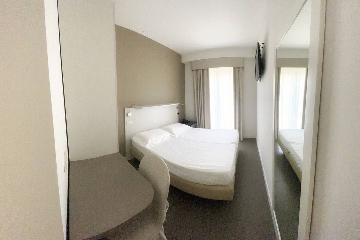 Hotellihuone, jossa on yksi sänky, pieni työpöytä ja peili.