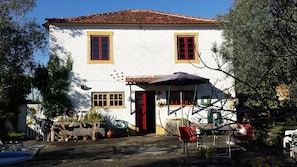 A two-story building with a red door and windows, surrounded by potted plants and outdoor furniture. - Beautiful country house in Monte Vale Grande. Very quiet rural area. (Soure)