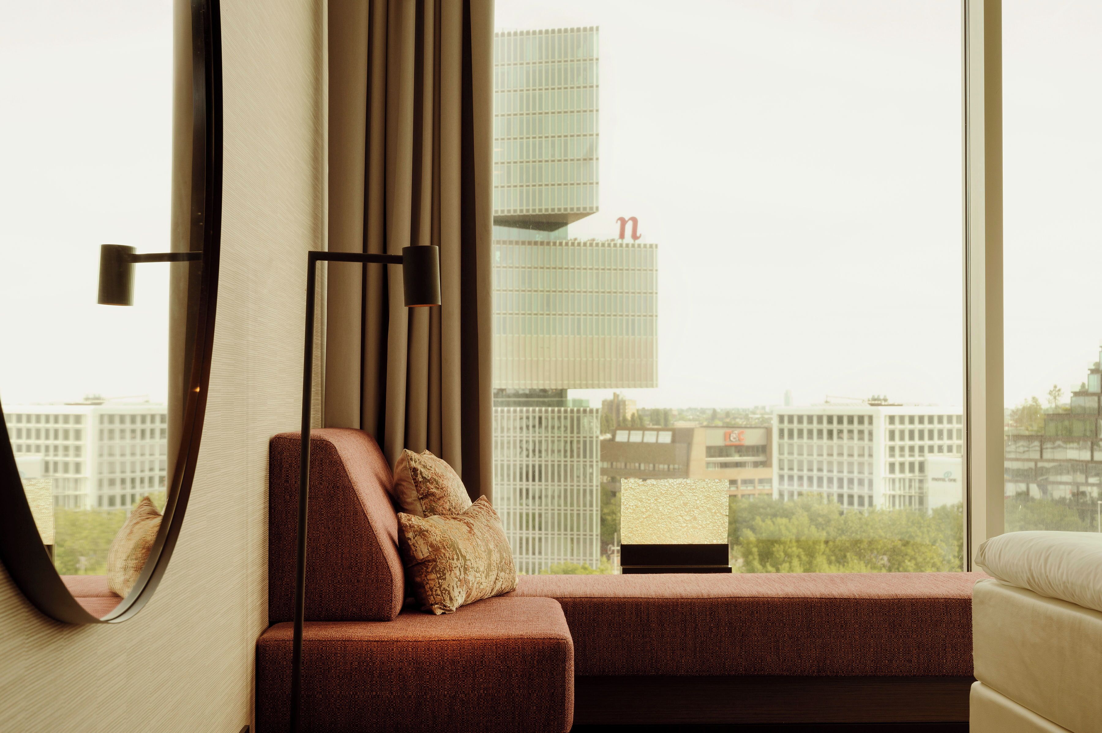 Une chambre d’hôtel moderne dotée d’une grande fenêtre, d’un canapé, d’un miroir et d’une lampe.