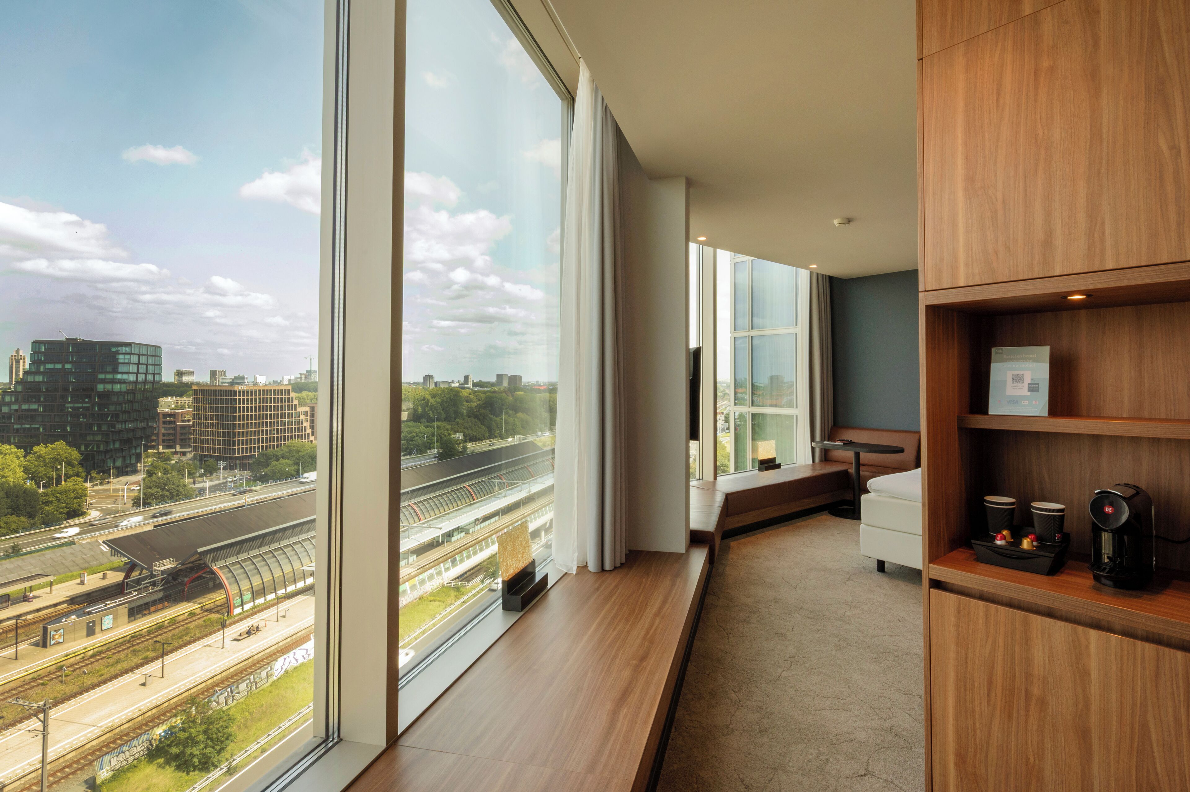 A modern hotel room with a large window offering a view of a cityscape and train tracks.