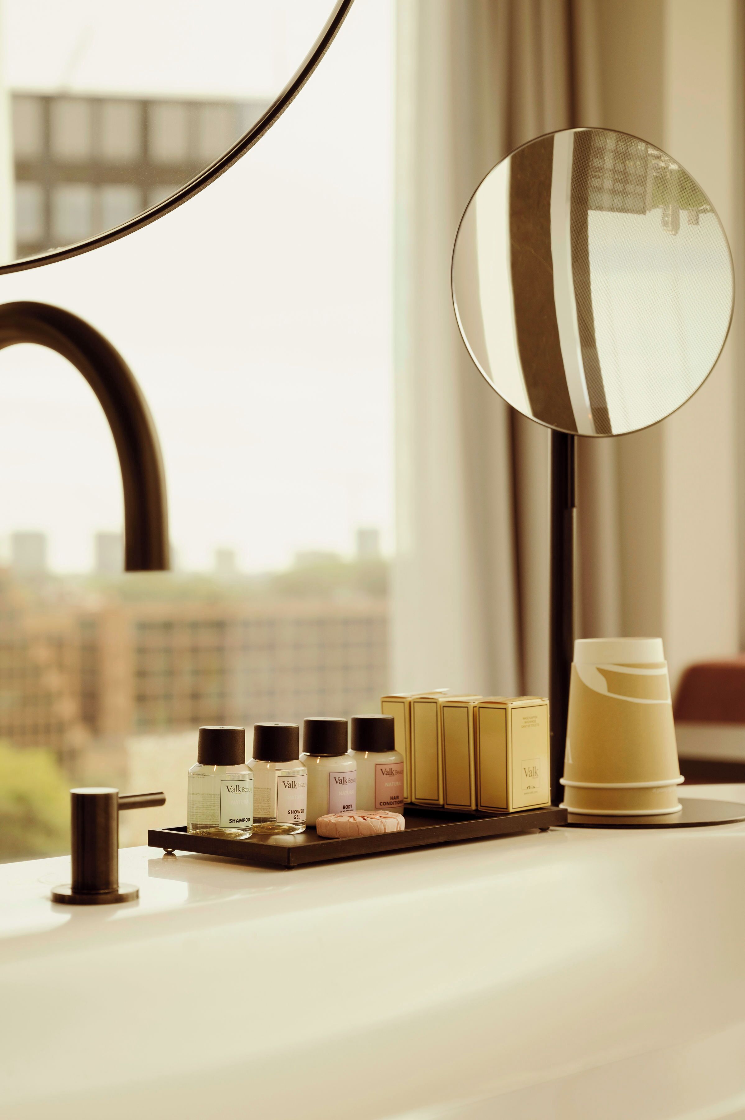 A bathroom vanity with a mirror, toiletries, and a view of the city.
