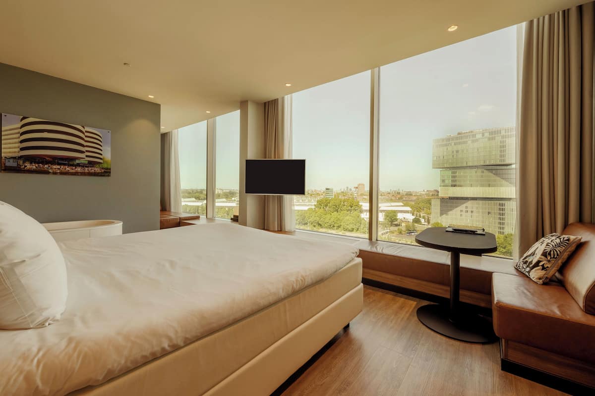 Een moderne hotelkamer met een groot bed, een televisie, een klein tafeltje en een bank.