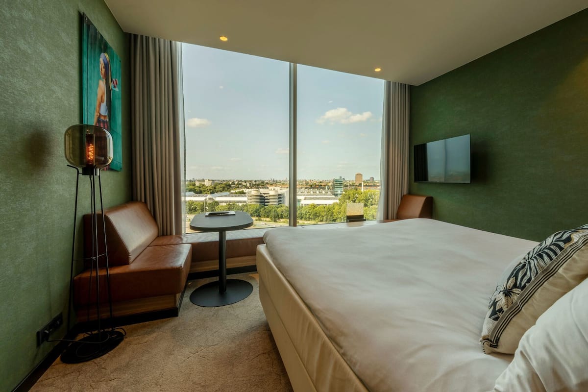 Een hotelkamer met een groot bed, een bank, een bijzettafeltje, een vloerlamp en een televisie.