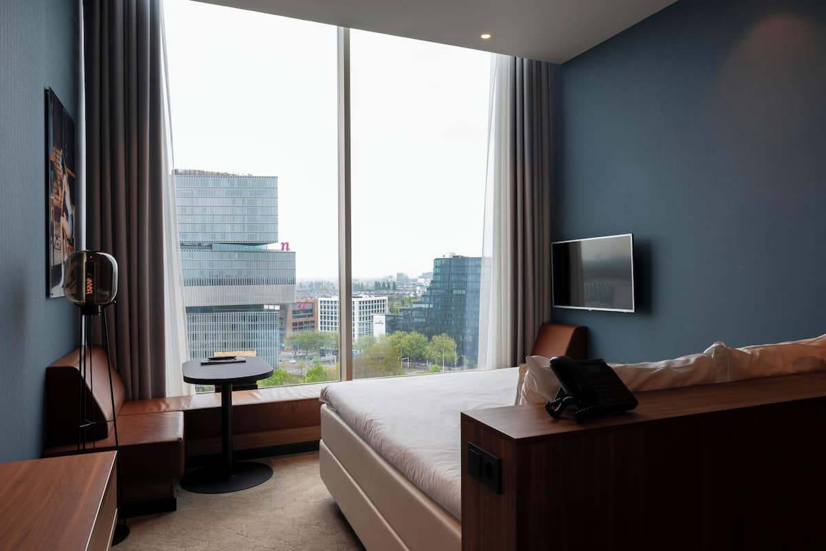 Een hotelkamer met een groot raam, een bed, een bureau, een stoel, een kleine tafel en een flatscreen-tv.