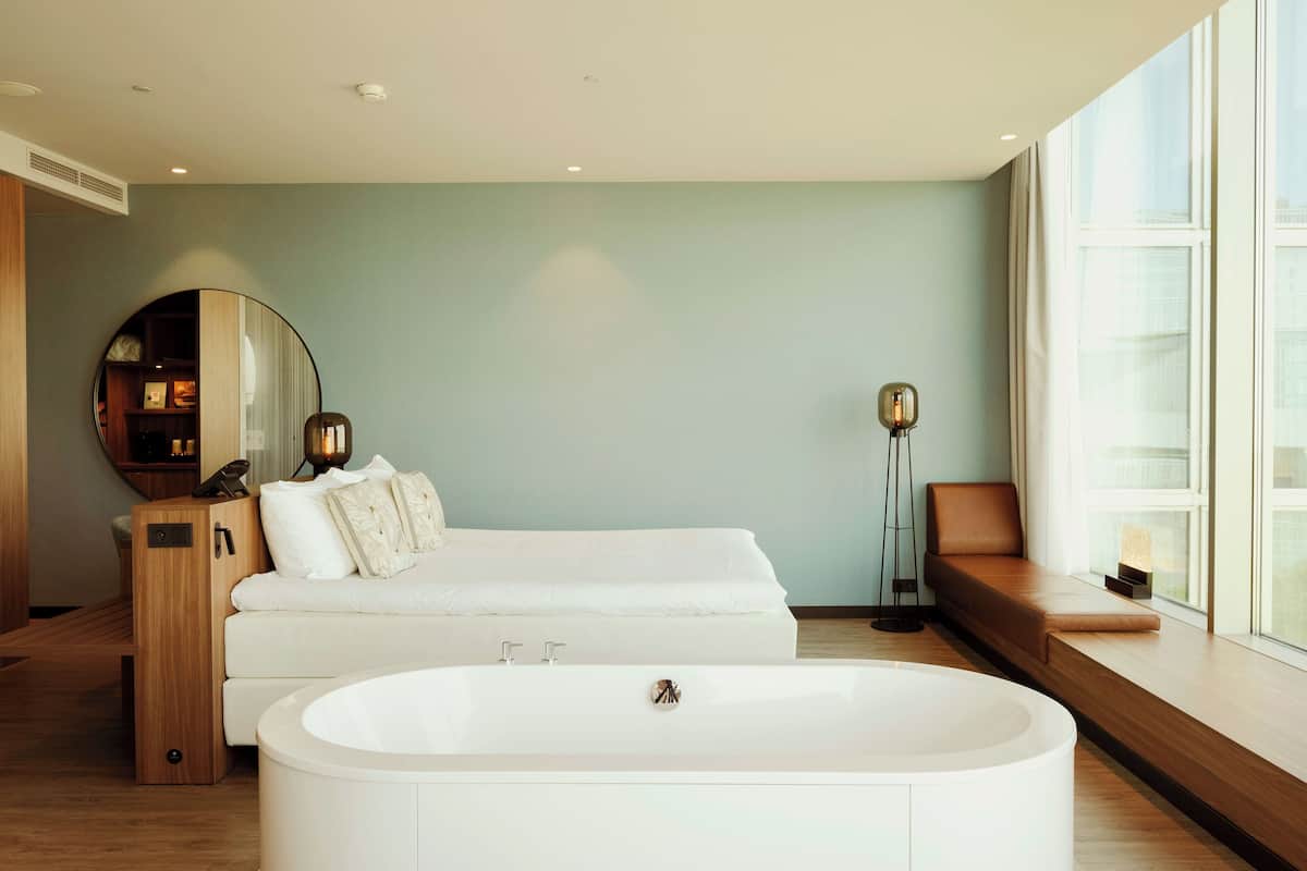 Een moderne badkamer met een vrijstaand bad, een wastafel met spiegel en een zithoek bij het raam.