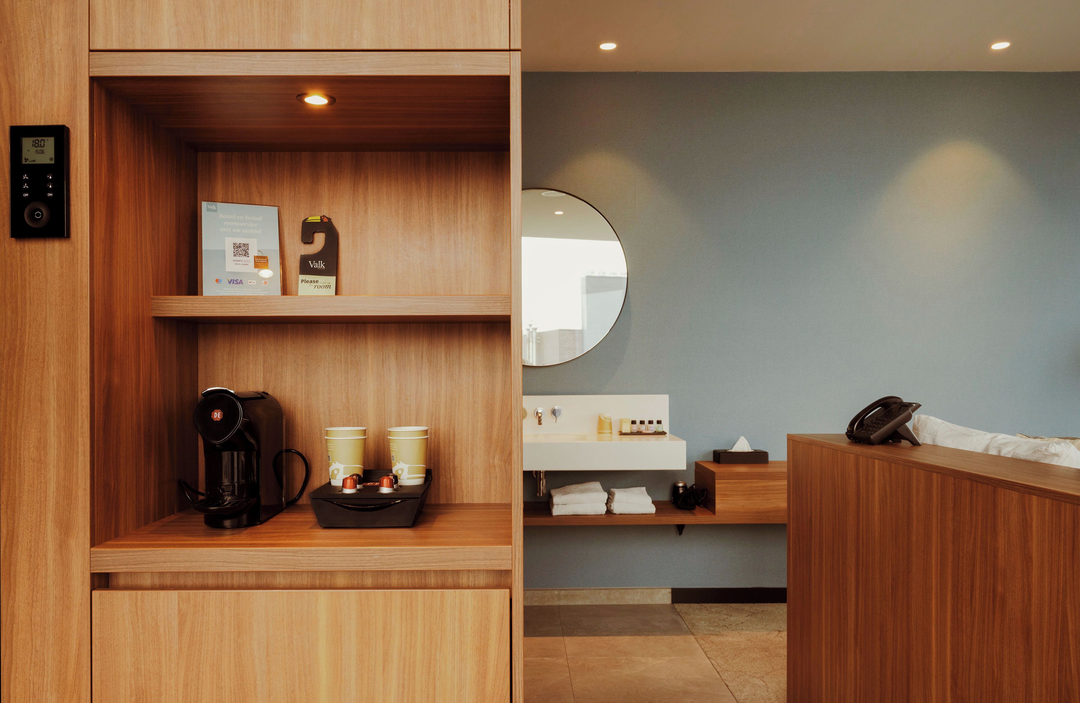 Habitació d'hotel moderna amb un taulell de recepció de fusta, una cafetera i un mirall a la paret.