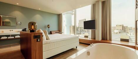 Une chambre d’hôtel moderne dotée d’une grande baignoire, d’un lit, d’une coiffeuse avec un miroir et offrant une vue sur la ville grâce à de grandes fenêtres.