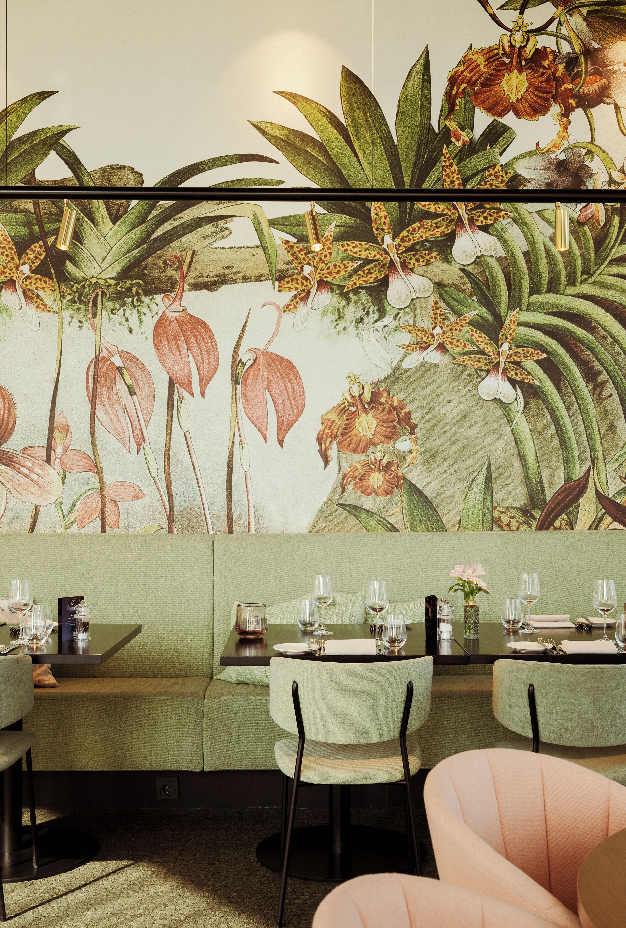 A restaurant with green upholstered booths, a mural of orchids, and a green and white color scheme.