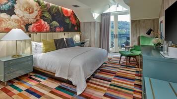 A bedroom with a large bed, a colorful striped rug, a green chair, and a view of the outdoors through a glass door.