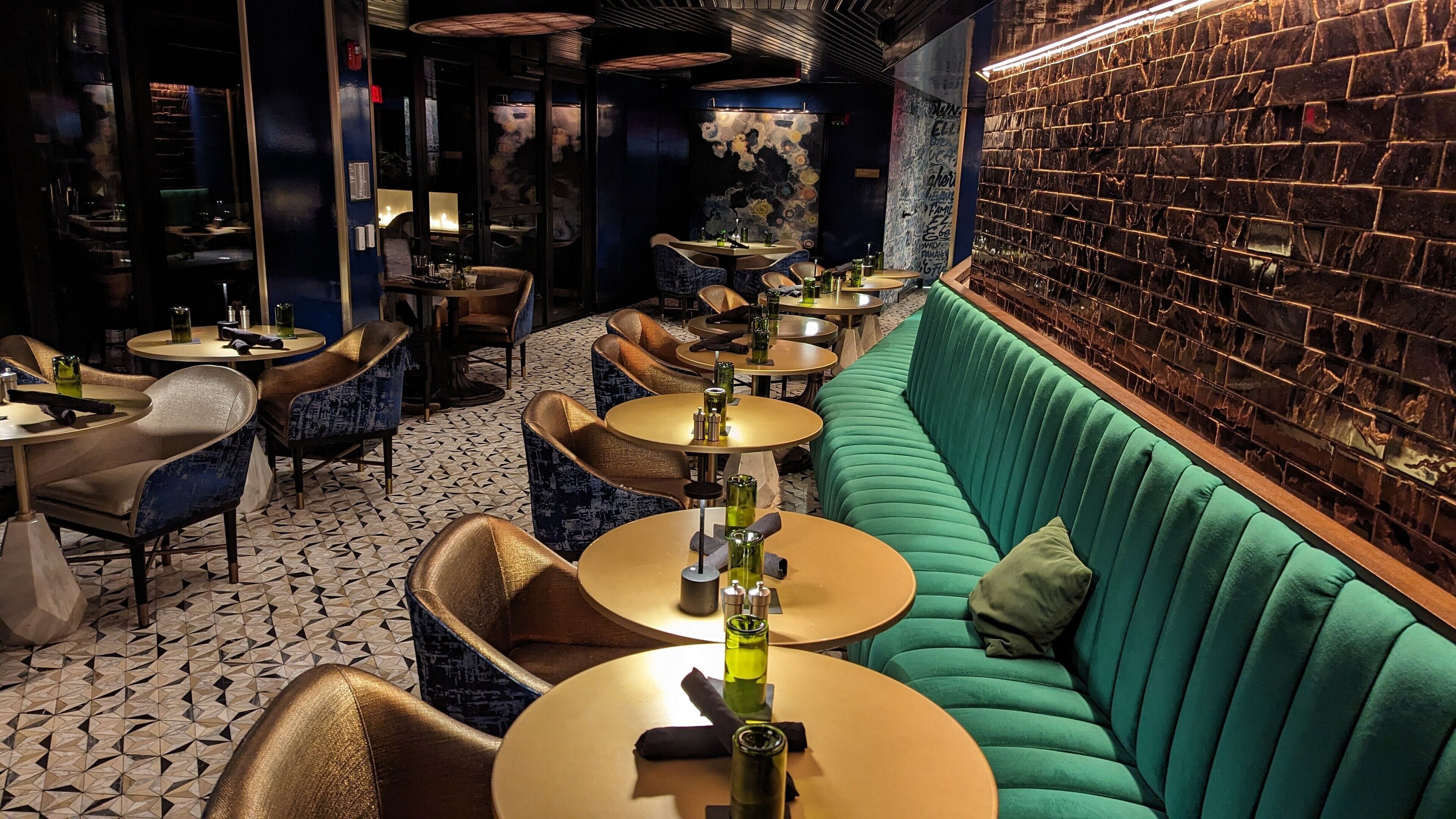 L’intérieur d’un restaurant avec des tables rondes, des chaises recouvertes d’un tissu bleu et un canapé vert.