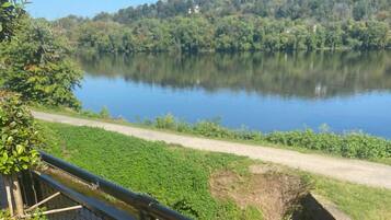 Vista de um lago com uma trilha de terra ao longo da margem, cercada por vegetação exuberante e árvores.