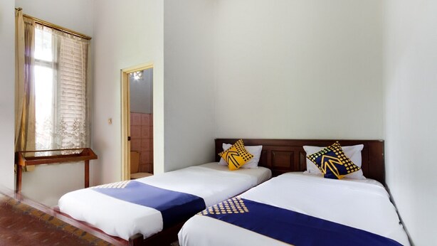 Quarto de hotel com duas camas de solteiro, janela com cortinas, cabeceira de madeira e uma porta.
