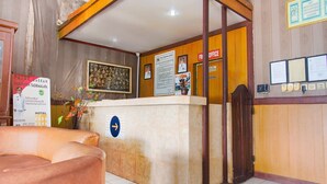 Uma área de recepção de hotel com balcão, um quadro na parede e a placa do hotel.