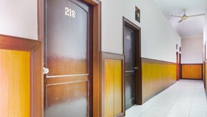 Corredor com portas de madeira numeradas 218 e 219, piso de azulejos brancos e um ventilador de teto.
