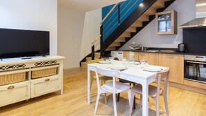 Une cuisine moderne dotée d’un four encastré, un coin repas avec une table et des chaises blanches, et un escalier agrémenté de touches de bleu.