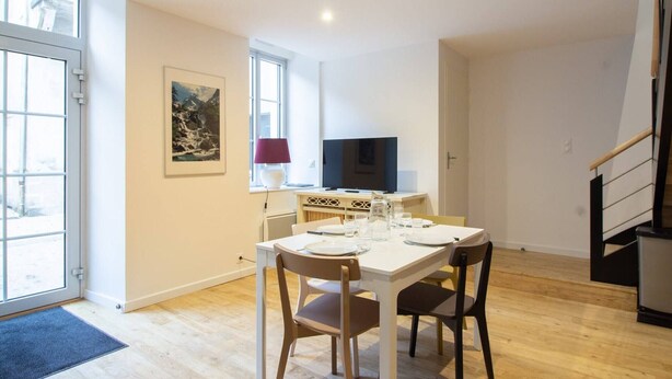 Un espace repas moderne avec une table et des chaises blanches, un téléviseur et un tableau accroché au mur.