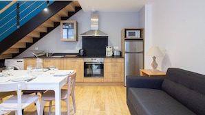 Une cuisine moderne avec des meubles en bois, une hotte de cuisinière en acier inoxydable, un four à micro-ondes et un réfrigérateur. On y trouve une table à manger avec des chaises, un canapé et un escalier avec des rampes bleues.