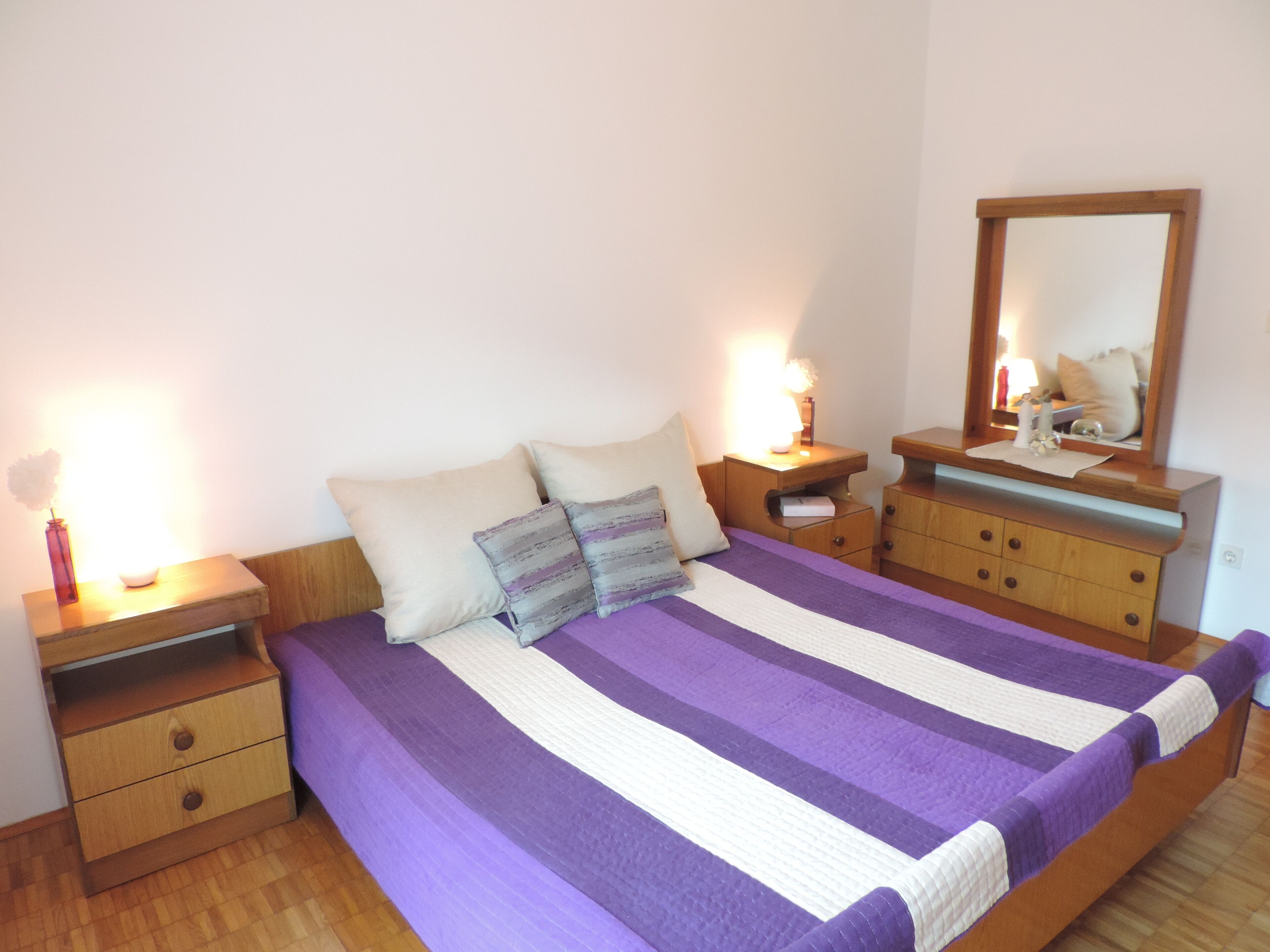 Een slaapkamer met een groot bed, houten nachtkastjes, een dressoir en een spiegel.