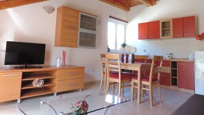 A modern kitchen with wooden cabinets, a dining area with chairs, a TV on a wooden stand, and a glass table with a bouquet. - Apartments Vodnica (Dubrovnik)