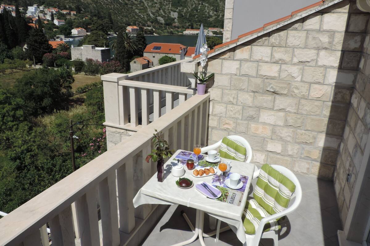 Un balcon avec une table préparée pour le petit-déjeuner, donnant sur une région montagneuse parsemée de maisons.